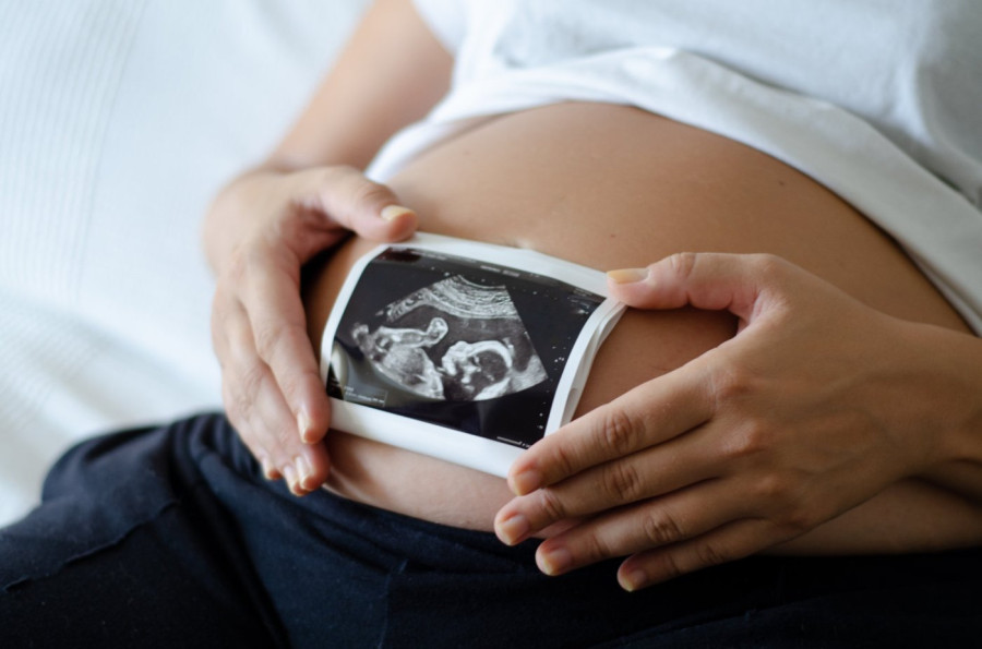 Pregnant woman holding ultrasound image over stomach