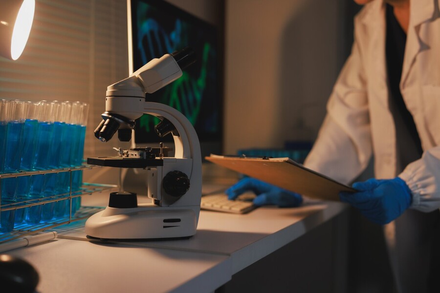 Person in lab coat and gloves, microscope